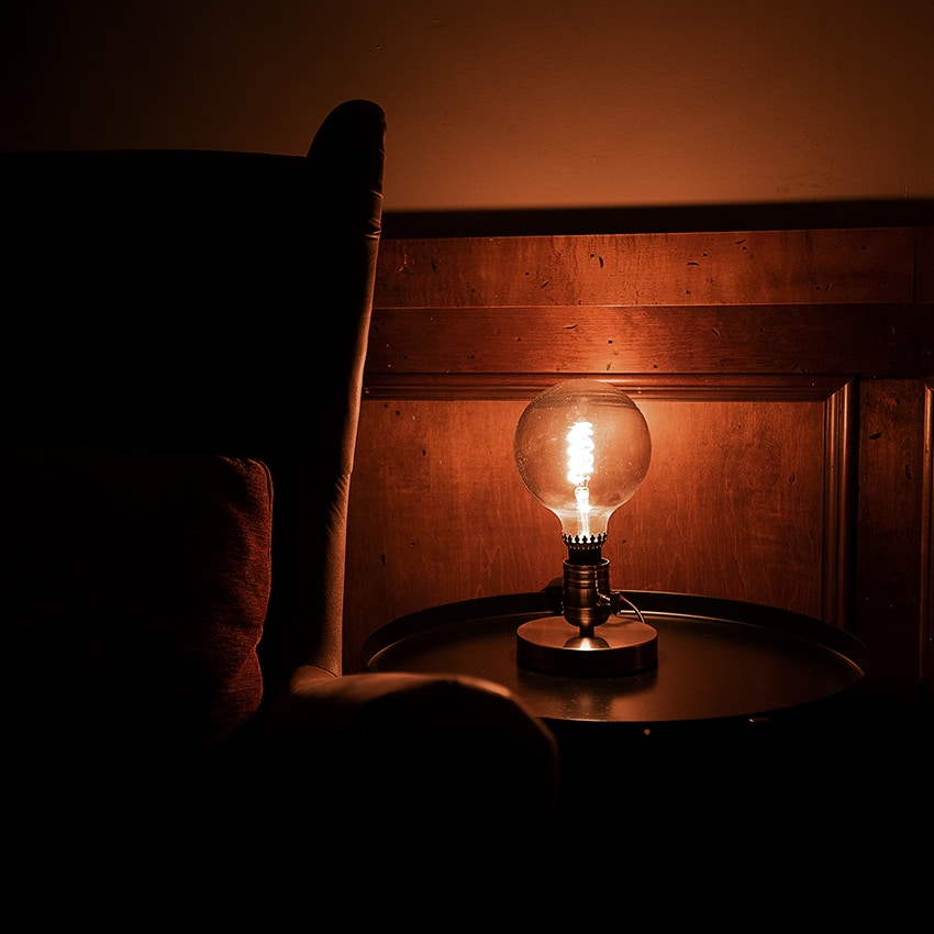 A single vintage lightbulb illuminating a side-table in a quiet dark corner of the restaurant