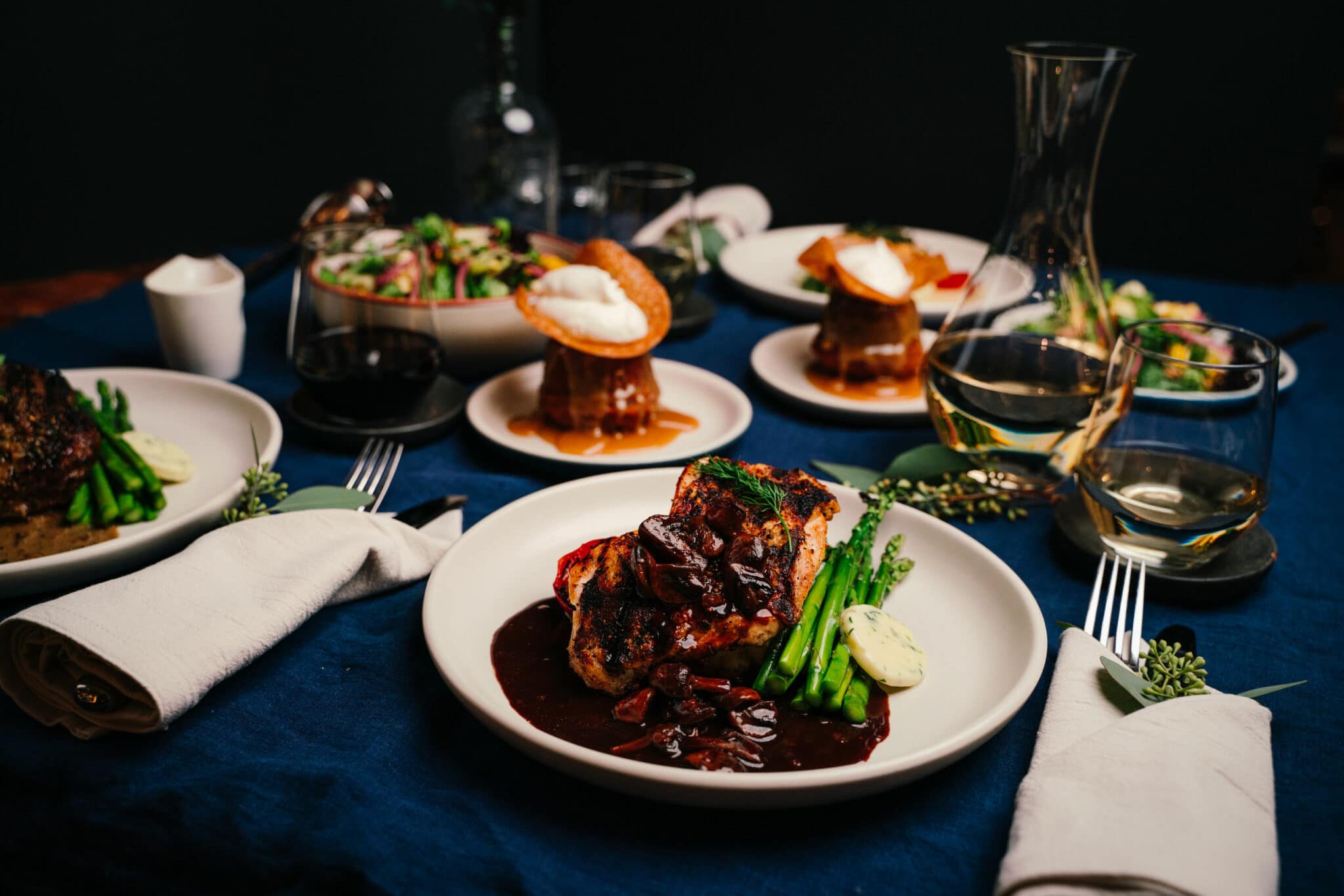 A full take-away heat-and-serve meal plated and paired with wine, laid out on a fancy table setting