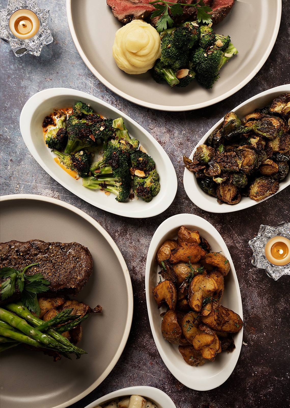 A top-down photo of five Saltlik dishes, including steaks, broccoli, brussels sprouts, and potato