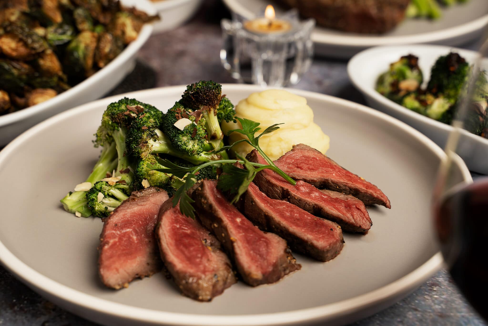 A Saltlik steak entree with mashed potato and broccoli, several sides in the background