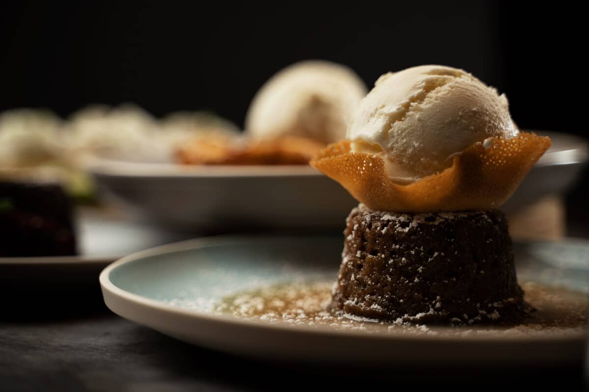 A dark and moody photo of a Saltlik dessert, a scoop of ice cream on a sugar wafer, on top of a sticky toffee pudding