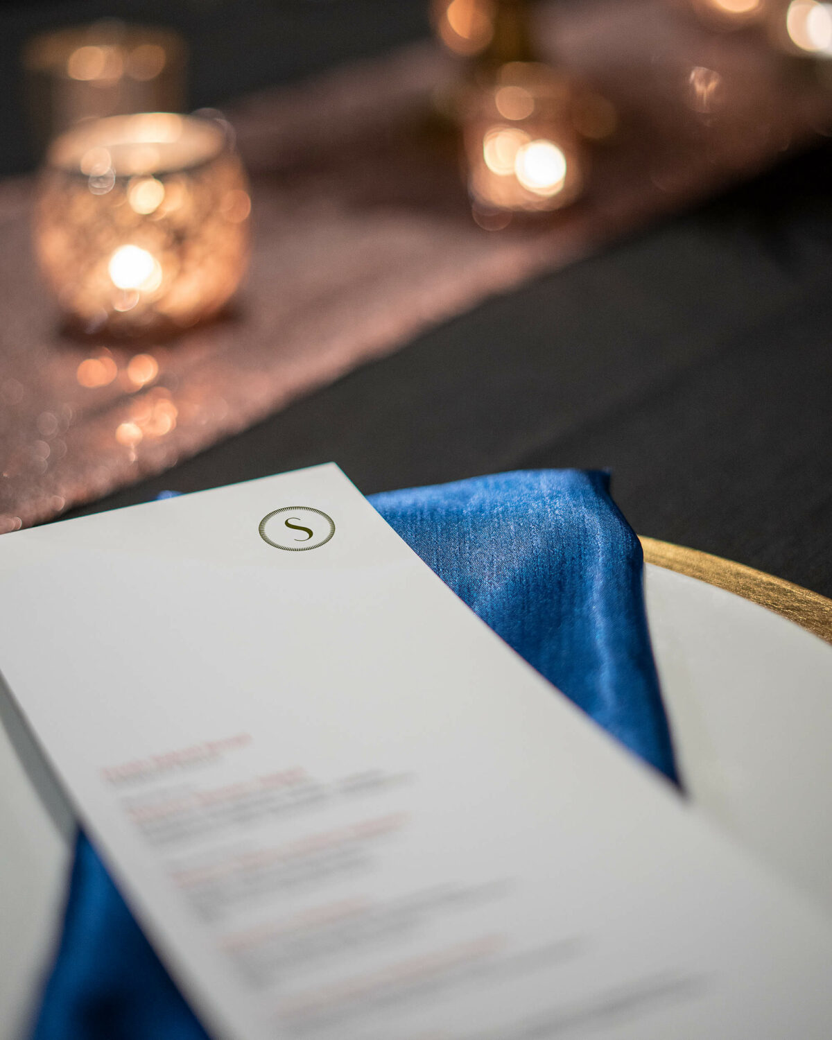 Saltlik event menu on top of a charger plate with a blue napkin, candle lit